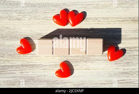 Reihe von vier leeren Holzblöcken, eingerahmt von roten Herzen auf einem Holzhintergrund. Beschriftungsvorlage. Stockfoto