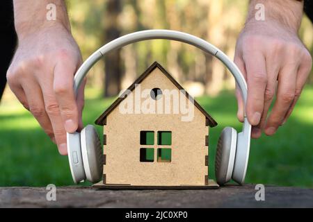 Mann, der weiße kabellose Kopfhörer auf ein kleines Holzhaus auf einem Baumstumpf legte. Konzept des Lebens in einer recht ländlichen Gegend. Stockfoto