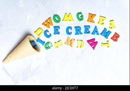 Aufschrift EIS aus einem Waffelkegel und bunten Holzbuchstaben auf einem konkreten Hintergrund angeordnet. Stockfoto