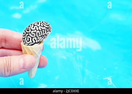 Hand hält eine anatomische Miniatur-Kopie eines menschlichen Gehirns in einem Waffelkegel, der ein Eis imitiert. Kreatives Gedankenerfrischungskonzept. Stockfoto