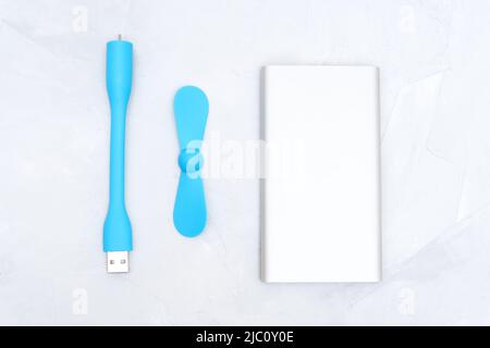 Tragbarer usb-Lüfter und eine schlanke silberne Powerbank, isoliert auf neutralem Hintergrund. Mobile Kühltechnologie. Stockfoto