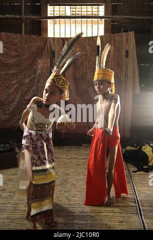 Kinder in traditioneller Trachtenkunst führen einen traditionellen Tanz während einer Ökotourismus-Veranstaltung im Longhouse der traditionellen Dayak IBAN-Gemeinde in Sungai Utik, Batu Lintang, Embaloh Hulu, Kapuas Hulu, West Kalimantan, Indonesien. Stockfoto