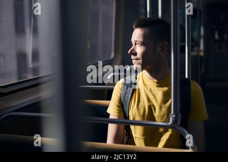 Nachdenklicher einsamer Mann, der aus dem Fenster des Zuges schaute. Alleinreisende in öffentlichen Verkehrsmitteln am sonnigen Tag. Stockfoto