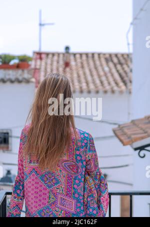 Blonde Frau von hinten auf dem Balkon mit Blick auf die ländliche Dorfstraße Stockfoto