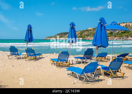 Liegestühle und Sonnenschirme am leeren Strand an sonnigen Tagen. Almyrida, Kreta, Griechenland Stockfoto