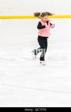 Kleine Mädchen, die Eiskunstlauf üben, bewegen sich auf der Indoor-Eisbahn. Stockfoto