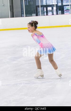 Kleines Mädchen, das Eiskunstlauf auf einer Indoor-Eisbahn übt. Stockfoto