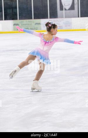 Kleines Mädchen, das Eiskunstlauf auf einer Indoor-Eisbahn übt. Stockfoto