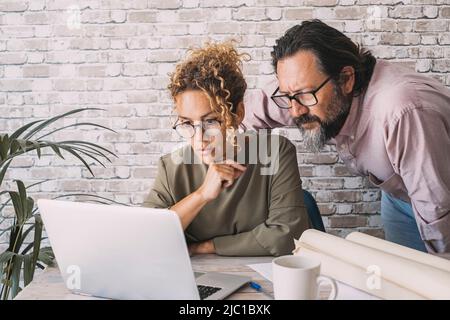 Mann und Frau arbeiten zusammen am Laptop im Heimbüro am Schreibtisch. Menschen und Online-Digital Job Business. Erwachsenes Paar, das mit Konzentra sucht Stockfoto