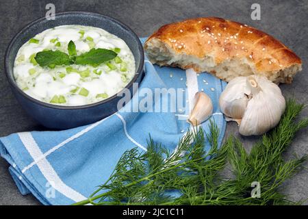 Mediterrane Küche. Tzatziki-Sauce aus frischen Gurken, Minze und Joghurt mit Zitrone und Knoblauch in einer dunklen Schüssel auf einem Betontisch Stockfoto