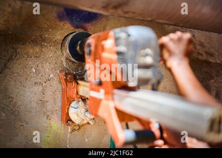 Bei einer Baustelle wird eine mit Wasser gespeiste Kernbohrmaschine verwendet, um eine Außenwand aus Beton zu durchschneiden. Stockfoto