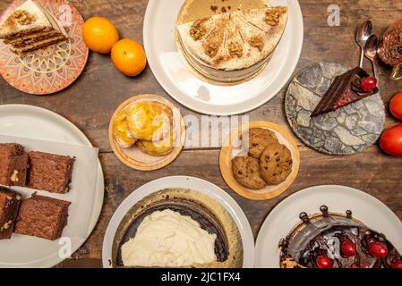 Set von süßen Desserts, Brownie, Orangen, Schlagsahne, Karottenkuchen, Schokolade- und Zuckerdonuts, kandierte Früchte, Pfannkuchen mit Sirup, Muffins, Chocola Stockfoto