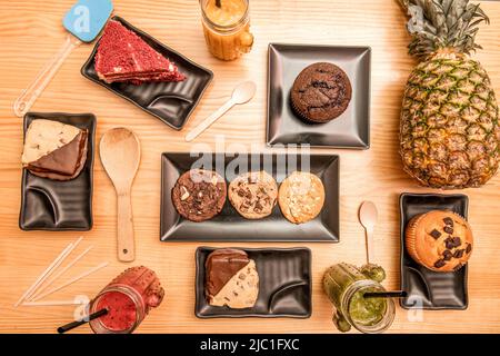 Set von süßen Desserts, Brownie, roten Samtkuchen, natürliche Ananas, Schokoladenkekse, Muffins und Smoothies Stockfoto