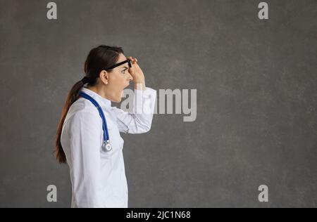 Schockiert und empört erhebt die Ärztin ihre Brille überrascht und blickt nach vorne. Stockfoto