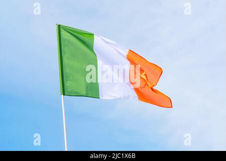 Irische Flagge winkt im Wind am frühen Morgen gegen einen blau bewölkten Himmel. Flagge Irlands Stockfoto