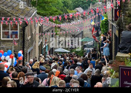 Haworth 1940er-Wochenende (geschäftiges, überfülltes Main Street Hill, dekoriert in rot-weiß-blauen Union Jacks, beliebter Familientag) - West Yorkshire, England, Großbritannien. Stockfoto