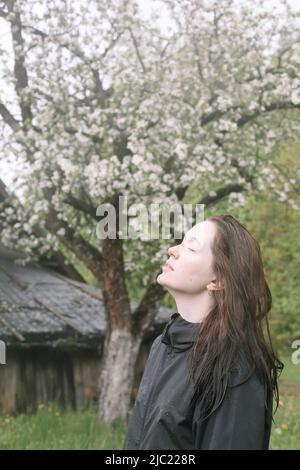 Emotionales Porträt einer jungen Frau, die im Frühling allein unter Regen im Freien steht. Stockfoto