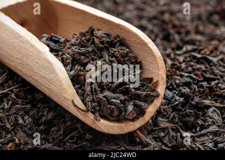 Trocknen Sie Tee mit langen Blättern in einer Holzlöffel. Makro von losem schwarzem Tee. Stockfoto