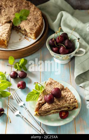 Hausgemachtes Sommergebäck glutenfrei. Schokoladen- und Quark-Kuchen mit Kirschen auf einem rustikalen Tisch. Stockfoto