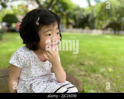 Schöne niedliche kleine Mädchen sitzt und machen eine Pose mit Lächeln im Garten mit Kopieplatz Stockfoto