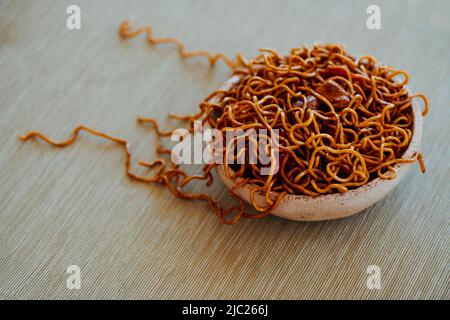 Nahaufnahme einer rustikalen Keramikplatte mit einigen Hühnchen-Yakisoba-Nudeln, auf einem Tischset mit einer beigen Tischdecke oder Tischdecke Stockfoto