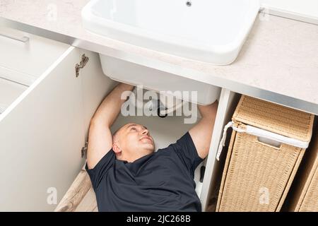 Draufsicht auf die Reparatur von Rohrleitungen durch einen Mann unter dem Waschbecken Stockfoto
