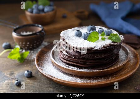 Pfannkuchen-Tag, Sommerdessert. Köstliche hausgemachte amerikanische Bananen-Schokoladen-Pfannkuchen mit Heidelbeeren auf einem rustikalen Tisch. Stockfoto