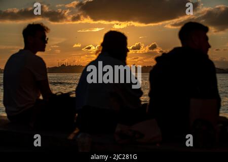 Istanbul, Türkei. 08.. Juni 2022. Silhouetten von Menschen, die während des Sonnenuntergangs auf dem Kadikoy Pier sitzen, mit einem Hintergrund der historischen Halbinsel. Der Sonnenuntergang in Istanbul schuf wunderschöne Bilder mit den Menschen, die in und um den Kadikoy-Dock gingen. Kredit: SOPA Images Limited/Alamy Live Nachrichten Stockfoto