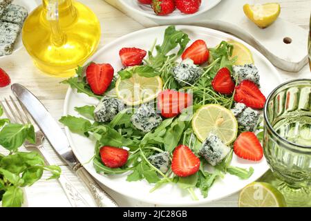 Salat mit Rucola, Blauschimmelkäse und Erdbeeren mit Weißwein auf weißem Hintergrund Stockfoto