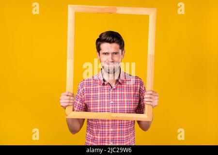 Portrait von attraktiven nervösen Kerl in den Händen halten Rahmen posiert isoliert über hellen gelben Hintergrund Stockfoto