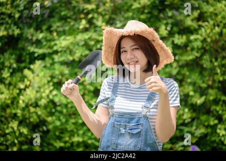 Eine asiatische Gärtnerin hält Gartengeräte in der Hand. Stockfoto