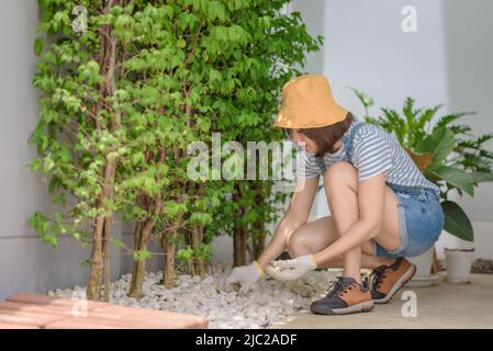 Eine asiatische Gärtnerin arrangiert einen Steingarten in ihrem Hinterhof. Stockfoto