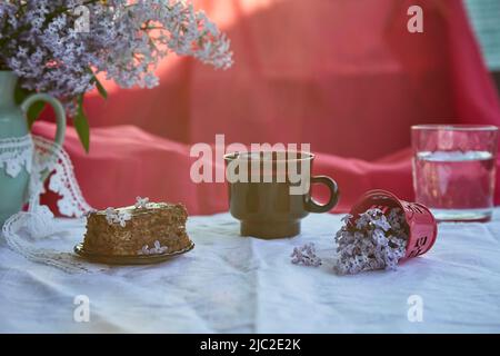 Süßer hausgemachter Schokoladenkuchen. Dessert und eine Tasse Kaffee zwischen Fliederblüten. Stimmungsvolles Frühstück. Speicherplatz kopieren. Stockfoto