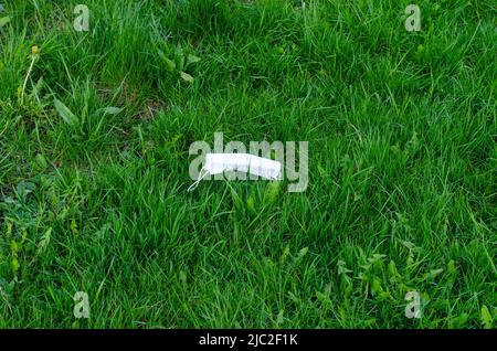 Weggeworfene medizinische Maske auf Gras. Umweltverschmutzung nach einer Coronavirus-Pandemie. Stockfoto