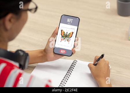 Asiatische Geschäftsfrau, die nft auf dem Smartphone erforscht, während sie sich im Büro Notizen macht Stockfoto