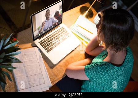 Kaukasische Geschäftsfrau Video ruft afroamerikanischen Geschäftsmann an, während sie spät im Büro arbeitet Stockfoto