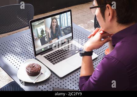 Glückliche kaukasische Geschäftsfrau winkt Hand über Videoanruf mit asiatischen männlichen Kollegen im Café sitzen Stockfoto