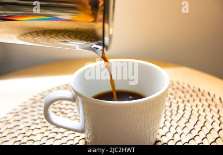 Kaffeefilter auf beige warmen Hintergrund. Ein Prozess, bei dem schwarzes Getränk in den weißen Becher gegossen wird. Ein Getränk, das zu Hause oder in einem Café im sonnigen Morni gemacht wird Stockfoto