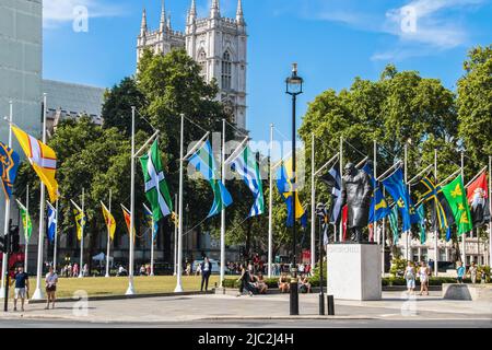 7-24-2019 London UK - Statue von Winston Churchill auf dem Parliament Square mit den Flaggen der Kronenabhängigkeiten und der Überseegebiete, die auf der Sonne fliegen Stockfoto