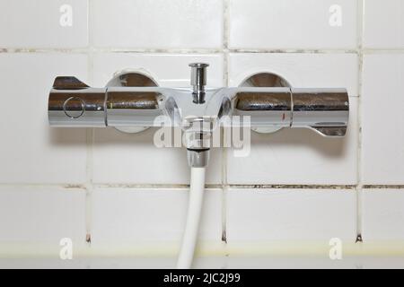 Mietschaden-Konzept: Duscharmatur über der Badewanne mit schwarzem Schimmel oder Pilz wächst auf Verkalkungen auf der Fliesenfuge. Stockfoto