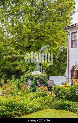 Charmanter Sitzbereich auf landschaftlich gestalteter Terrasse außerhalb des zweistöckigen Stuckhauses mit weiter Einrichtung und Kürbis - verschwommene Bäume im Hintergrund Stockfoto