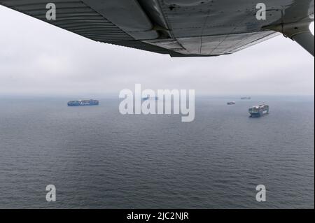 Hamburg, Deutschland. 09.. Juni 2022. Das Containerschiff Evergreen (r) liegt neben anderen Frachtern und Containerschiffen von COSCO Shipping unter anderem in der Nordsee vor Anker. Dutzende Schiffe liegen in der Deutschen Bucht vor Anker und warten auf die Räumung, da die Containerschifffahrt aufgrund der Corona-Pandemie vom Kurs abgeworfen wird. Ein Teil des Flügels des Flugzeugs ist oben im Bild zu sehen. Quelle: Jonas Walzberg/dpa/Alamy Live News Stockfoto