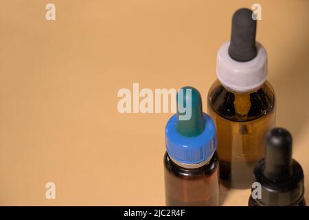 Braune Flaschen mit Droppern, ohne Branding, Textraum, gelblicher Hintergrund. Stockfoto