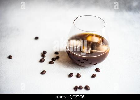 Nahaufnahme eines eisgekühlten Kaffeegetränks auf einem Tisch mit gerösteten Kaffeebohnen Stockfoto