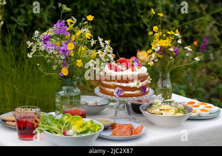 Skandinavisches Mittsommergericht mit Erdbeer- und Cremekuchen, Kartoffelsalat, Lachs und Eiern Stockfoto