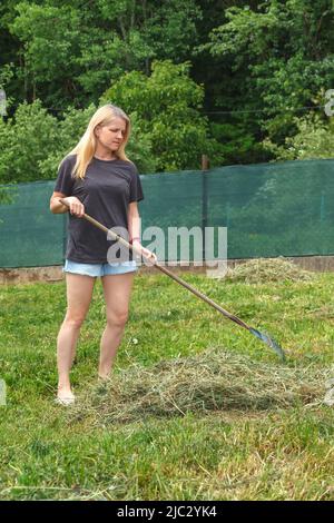 Mädchen sammelt trockenes Gras mit Gartenrechen Stockfoto