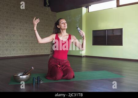 Eine Frau, die Yoga praktiziert, mit Weihrauch meditiert, auf einer Matte im Raum sitzt Stockfoto