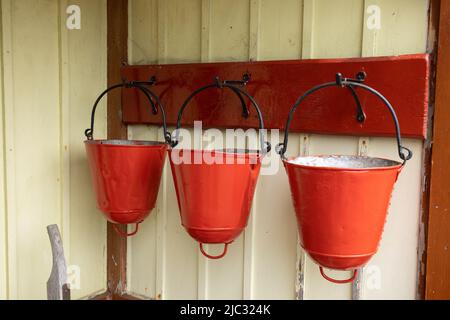 Drei traditionelle Feuereimer hängen an einer gelben Holzwand am Bahnhof von Bolton Abbey, Yorkshire, Großbritannien Stockfoto