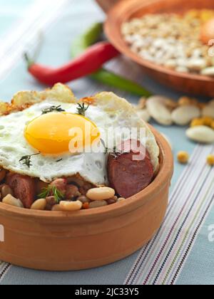 Ein traditioneller griechischer Dorfteller mit gebackenen Bohnen, gegrillter Wurst, Kräutern und einem Spiegelei auf der Oberseite Stockfoto