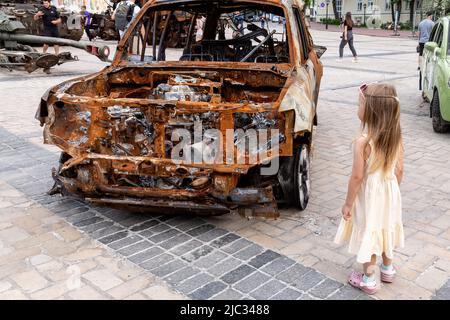 Kiew, Ukraine. 09.. Juni 2022. Ein Mädchen sieht ein verbranntes Auto während einer Ausstellung zerstörter ukrainischer Bürgerwagen und russischer Kriegsfahrzeuge, die am 9. Juni 2022 auf dem Michailovskyi-Platz in der Altstadt von Kiew, Ukraine, ausgestellt wurden. Als die Russische Föderation vor 3 und einem halben Monat in die Ukraine einmarschierte, dauern die heftigen Kämpfe im Osten des Landes an. Die Hauptstadt Kiew bleibt in relativer Sicherheit, obwohl in der ganzen Stadt Erinnerungen an den Krieg wie schützende Sandsäcke, Straßensperren, nationale und Anti-Kriegs-Symbole zu sehen sind. (Foto von Dominika Zarzycka/Sipa USA) Quelle: SIPA USA/Alamy Live News Stockfoto